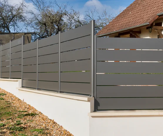 Clôture en aluminium gris à lames pleines, posée en escalier sur un muret en pente